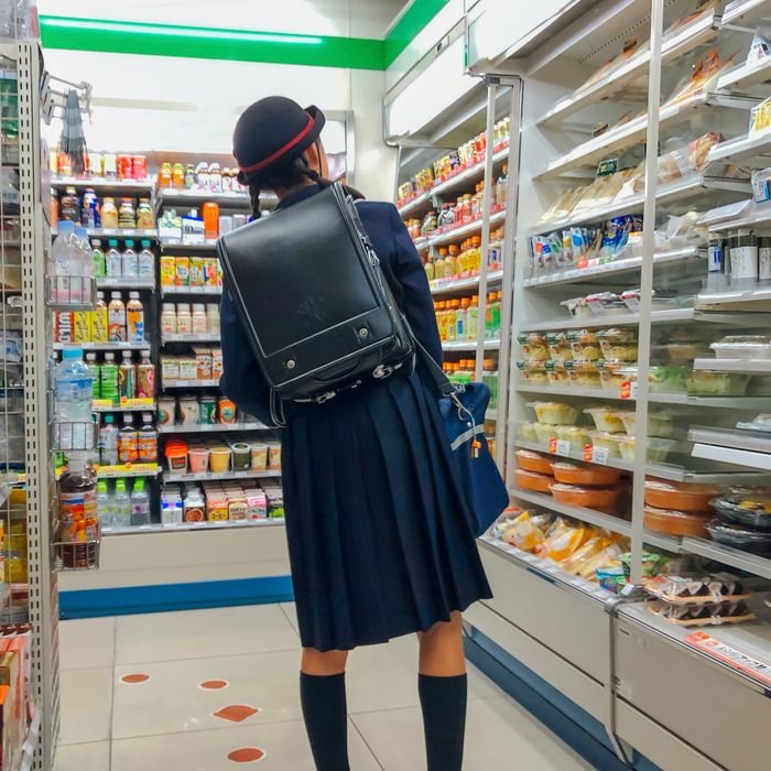 A student in uniform browsing snacks in a convenience store aisle indoors.